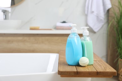 Wooden tray with bottles of shower gels and bath bomb on tub indoors, space for text