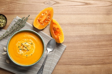 Photo of Flat lay composition with pumpkin cream soup in bowl on wooden background. Space for text