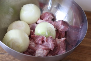 Photo of Fresh raw meat and ripe onions in bowl on wooden table, closeup