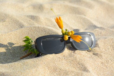 Photo of Stylish sunglasses and tropical flower on sand, closeup