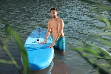 Photo of Man standing near SUP board in river water on sunny day