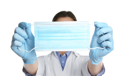 Photo of Doctor in latex gloves holding disposable face mask on white background, closeup. Protective measures during coronavirus quarantine