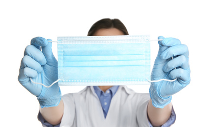 Doctor in latex gloves holding disposable face mask on white background, closeup. Protective measures during coronavirus quarantine