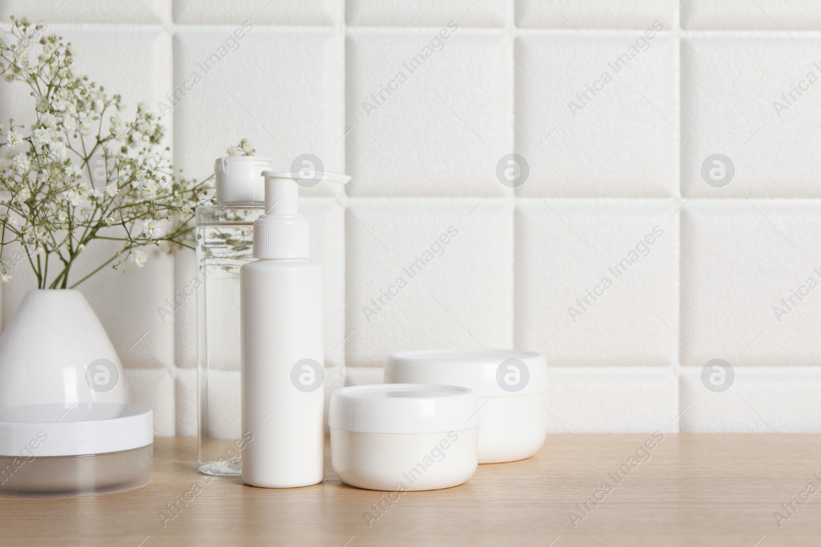 Photo of Bath accessories. Different personal care products and gypsophila flowers in vase on wooden table near white tiled wall, space for text