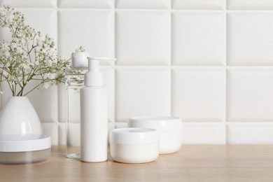 Bath accessories. Different personal care products and gypsophila flowers in vase on wooden table near white tiled wall, space for text