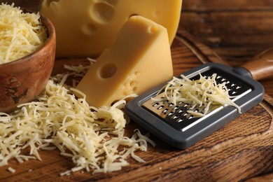 Photo of Grated, cut cheese and grater on wooden table, closeup