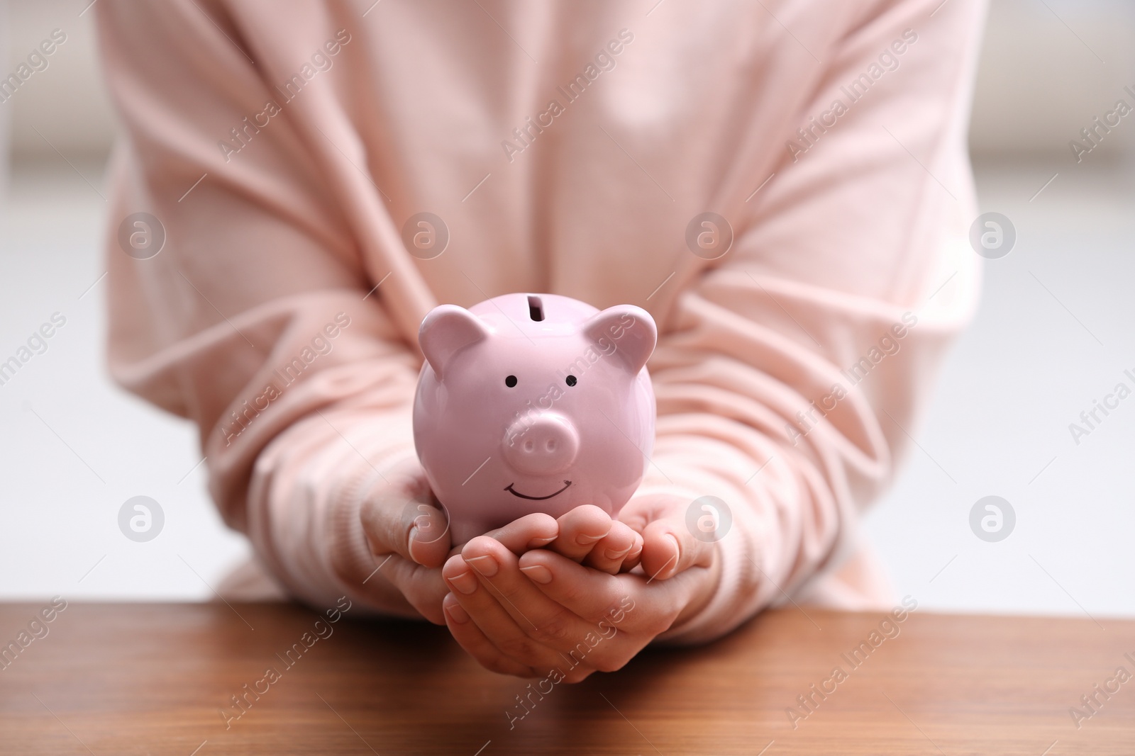 Photo of Woman with piggy bank at wooden table, closeup