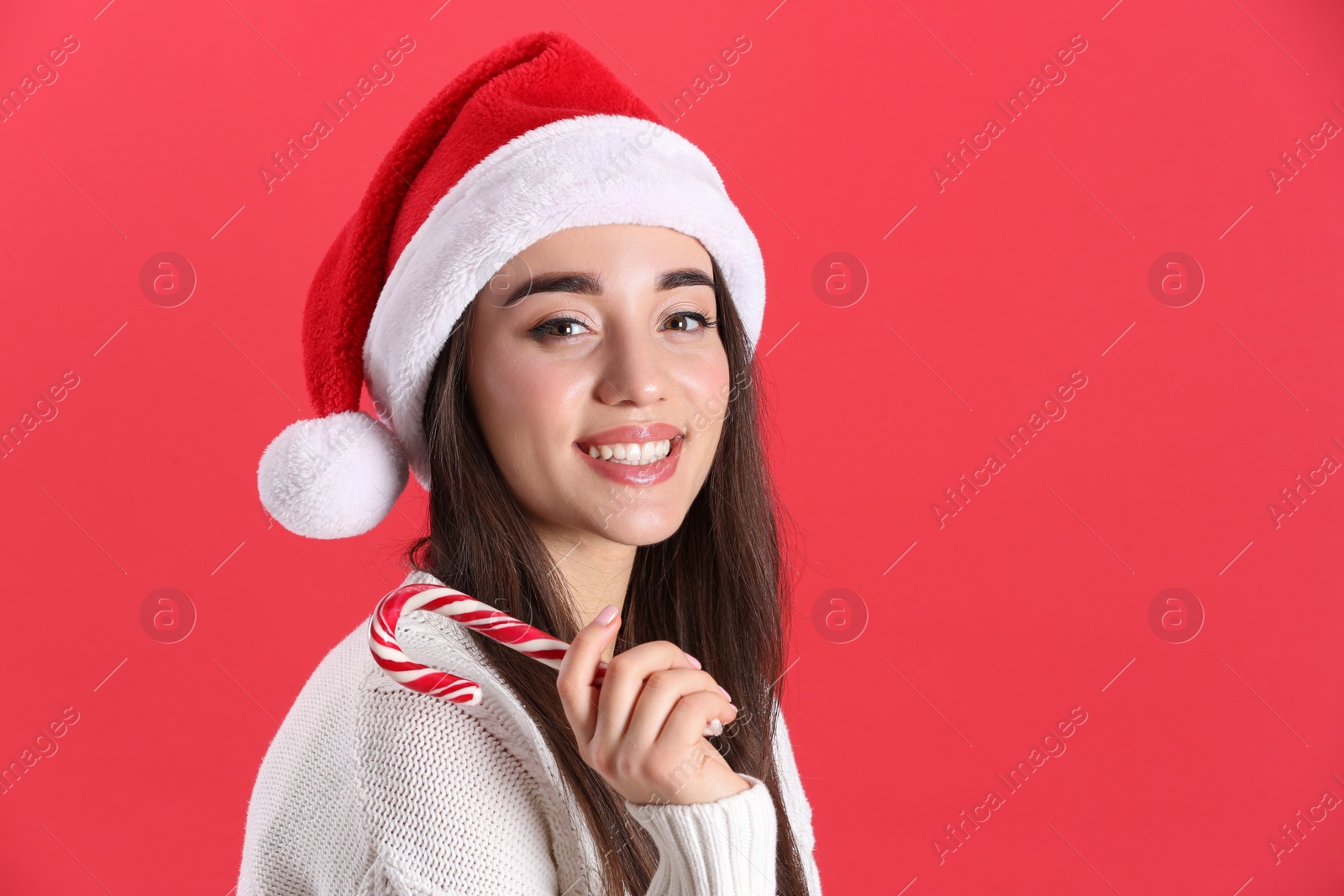 Photo of Beautiful woman in Santa Claus hat holding candy cane on red background. Space for text