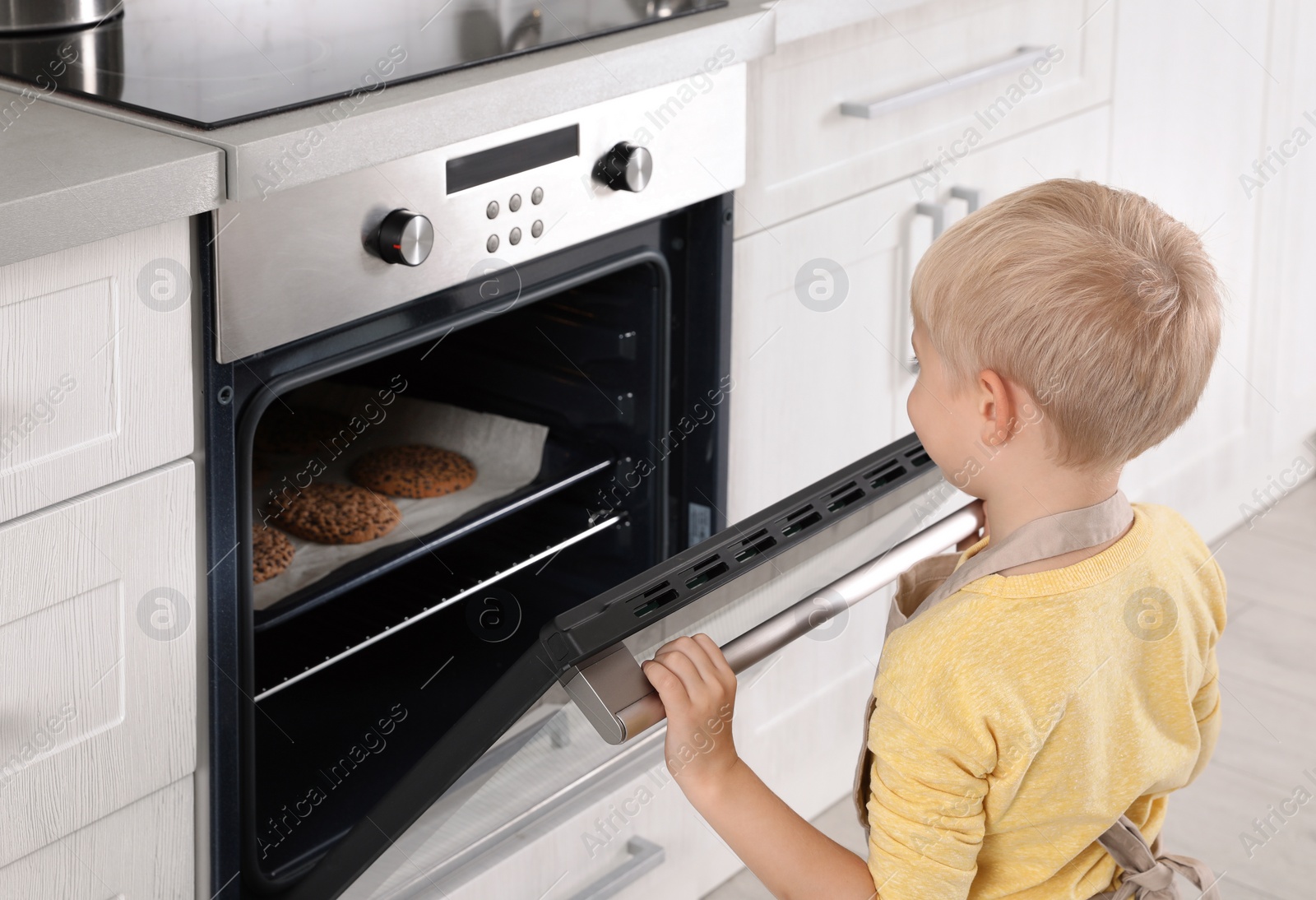 Photo of Little boy baking cookies in oven at home