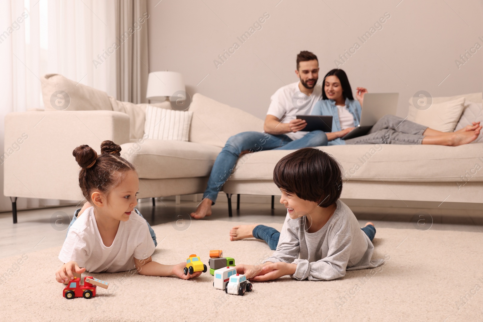 Photo of Cute children playing with toys while parents using gadgets on sofa in living room