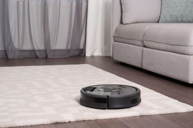 Photo of Hoovering floor with modern robotic vacuum cleaner in living room