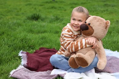 Little girl with teddy bear on plaid outdoors. Space for text