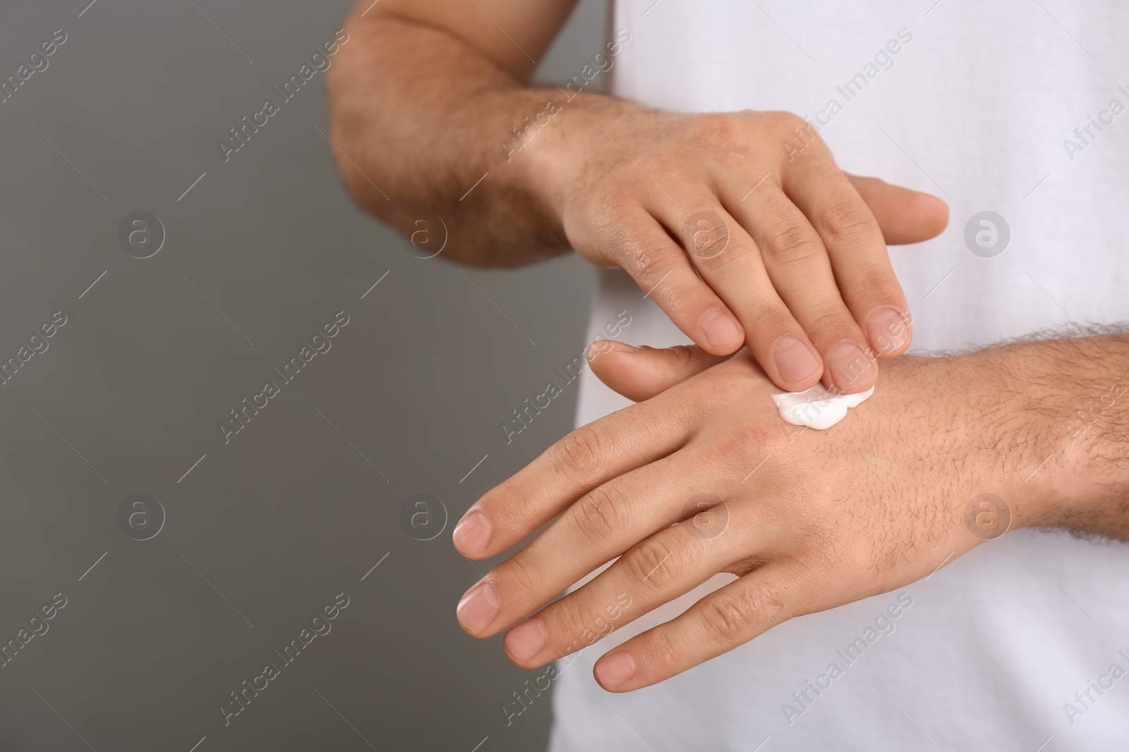 Photo of Man applying cream onto hand on grey background, closeup