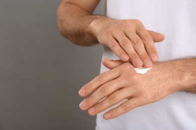 Photo of Man applying cream onto hand on grey background, closeup