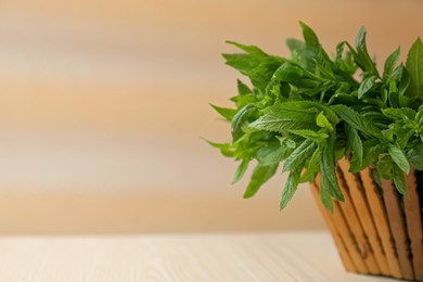 Photo of Beautiful green mint in basket on white wooden table, closeup. Space for text