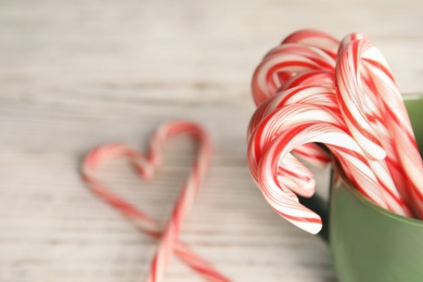Photo of Tasty candy canes in cup on wooden table. Space for text
