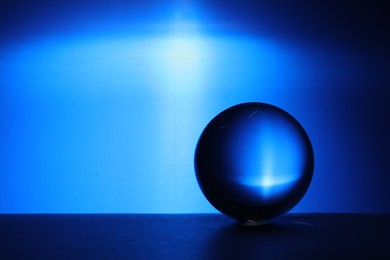 Photo of Transparent glass ball on table against blue background. Space for text