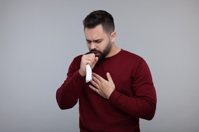 Photo of Sick man with tissue coughing on gray background