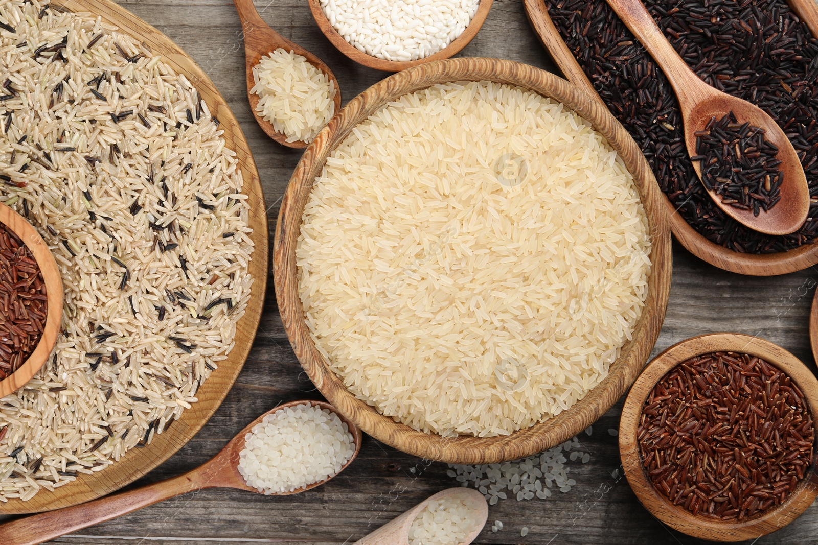 Photo of Different sorts of rice on wooden table, flat lay