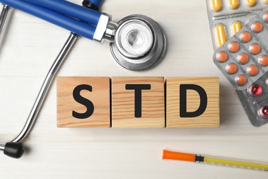 Photo of Abbreviation STD made with cubes, drugs and stethoscope on white wooden table, flat lay