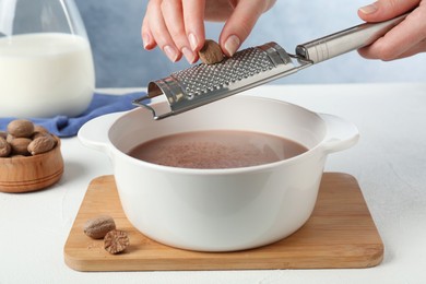 Photo of Woman grating nutmeg into cacao at table, closeup