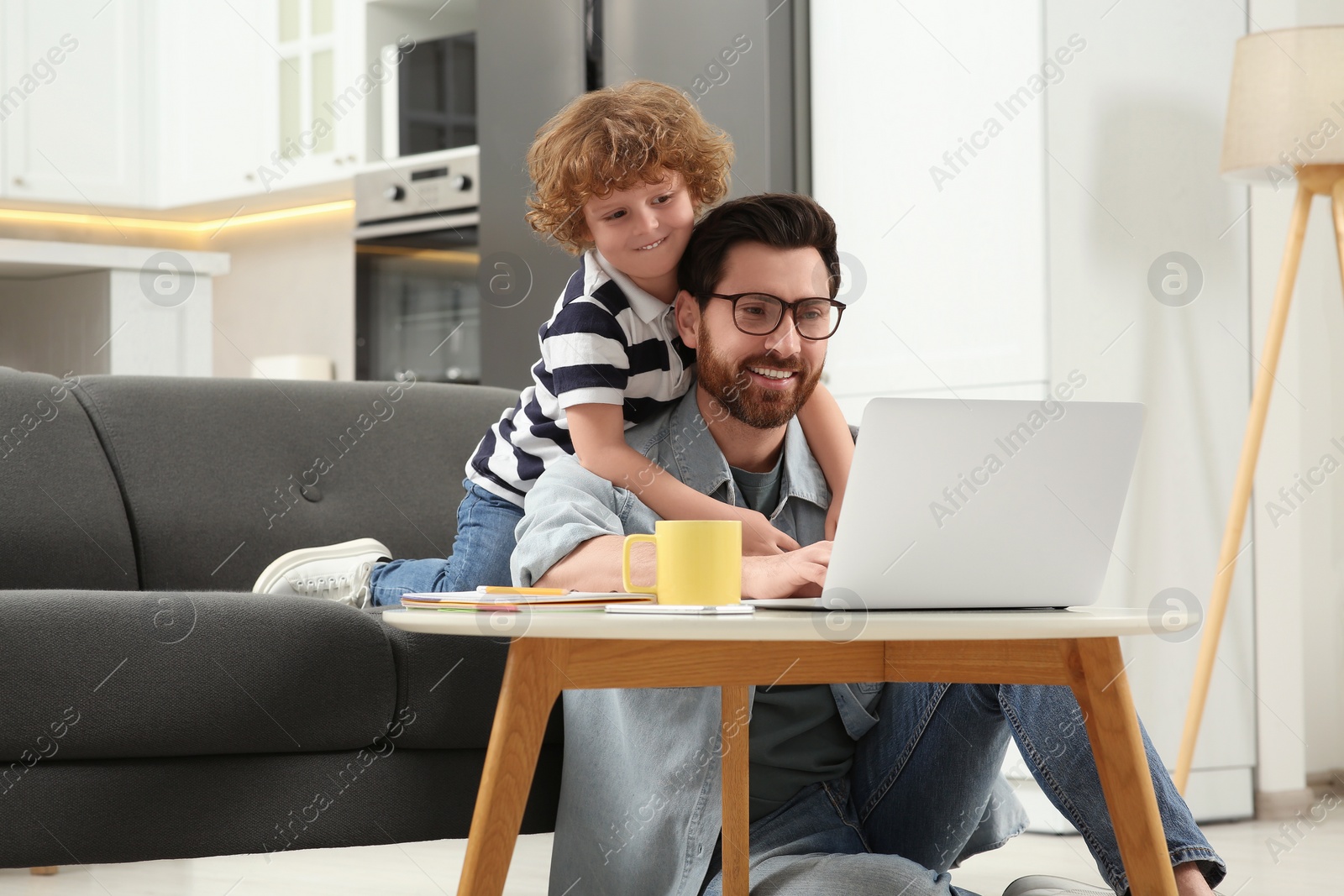 Photo of Man with laptop working remotely at home. Father and son at desk