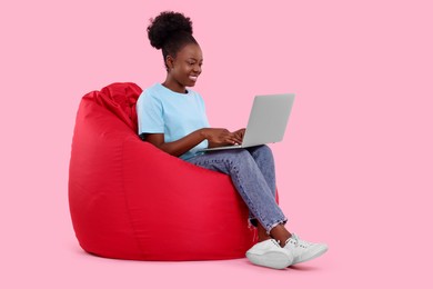 Photo of Beautiful young woman with laptop sitting on beanbag chair against pink background