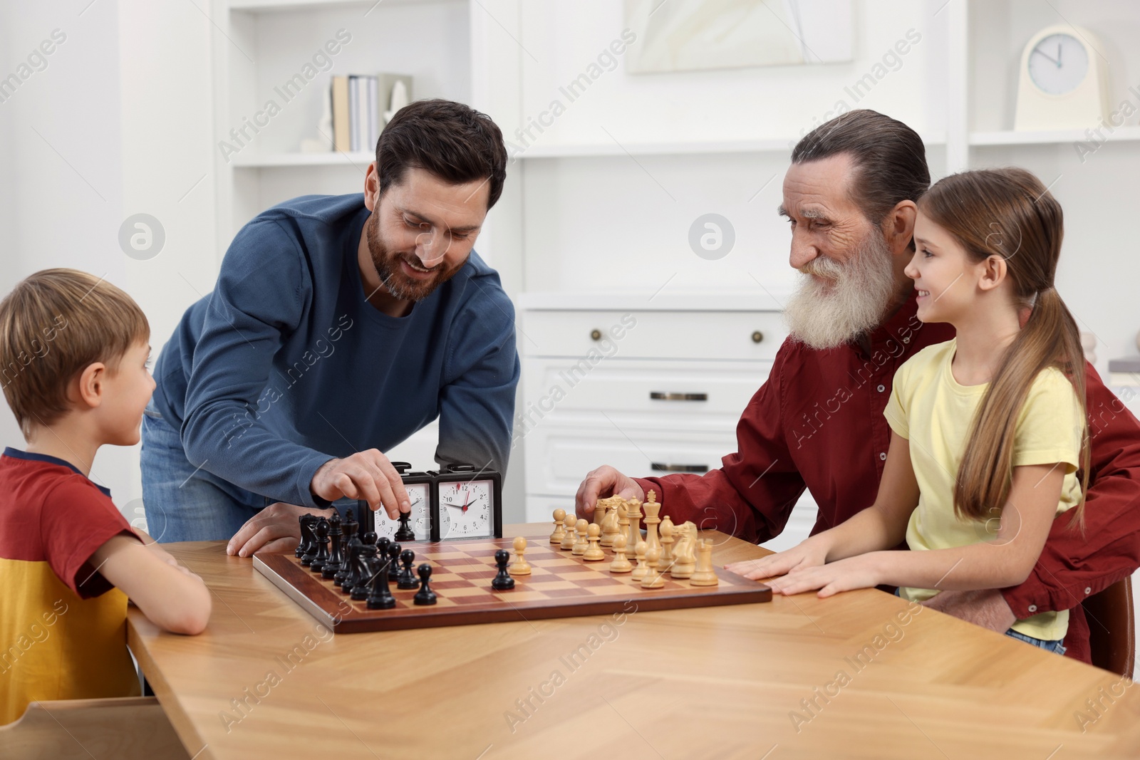 Photo of Family playing chess together at table in room