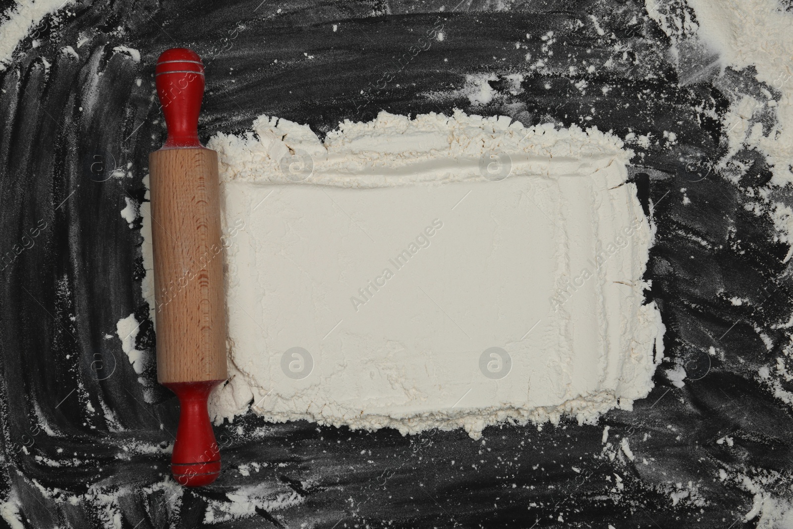 Photo of Flour and rolling pin on black table, top view. Space for text