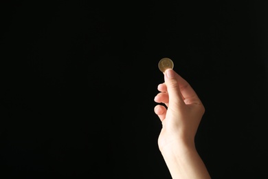 Young woman holding coin on black background, closeup view. Space for text