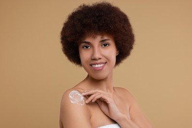Photo of Beautiful young woman applying body cream onto shoulder on beige background