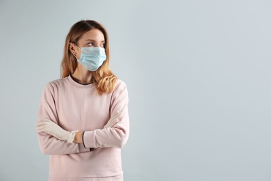 Young woman in medical gloves and protective mask on grey background. Space for text
