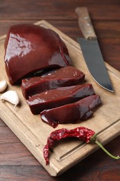 Photo of Cut raw beef liver with chili pepper, garlic and knife on wooden table, closeup