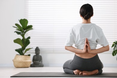 Girl practicing vajrasana with namaste behind back on mat in yoga studio