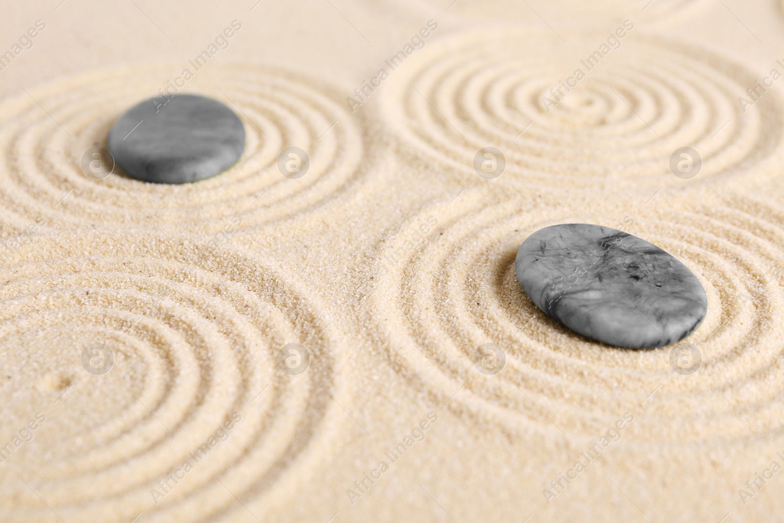 Photo of Zen garden stones on beige sand with pattern, closeup