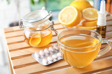 Cup with hot tea, honey and pills for cold on wooden table