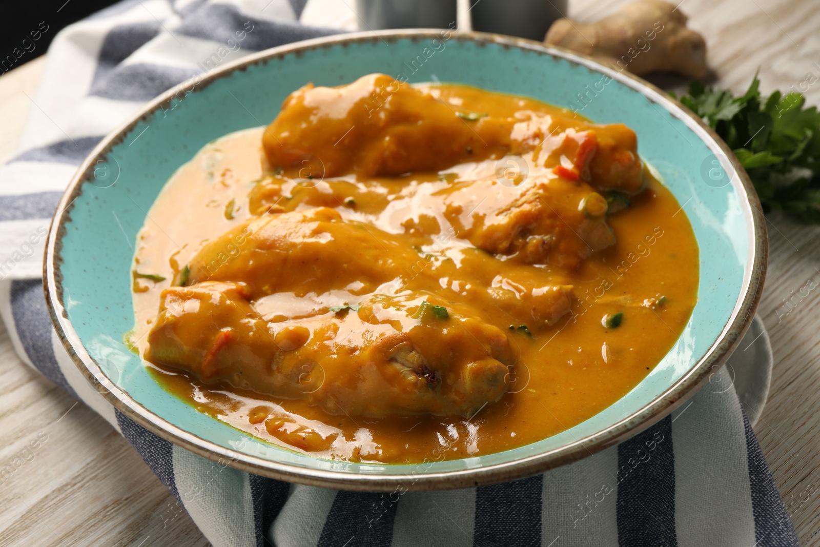 Photo of Tasty chicken curry, parsley and ginger on wooden table, closeup