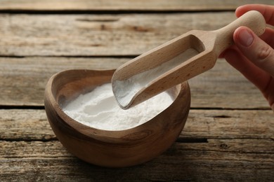 Photo of Woman taking baking powder with scoop from bowl at wooden table, closeup