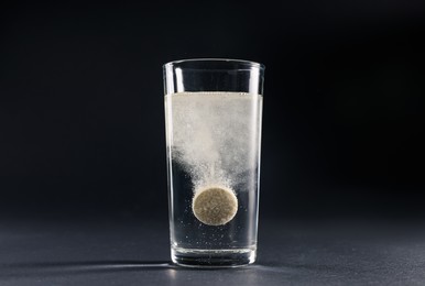 Effervescent pill dissolving in glass of water on grey table