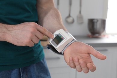 Young man checking pulse with digital medical device indoors, closeup