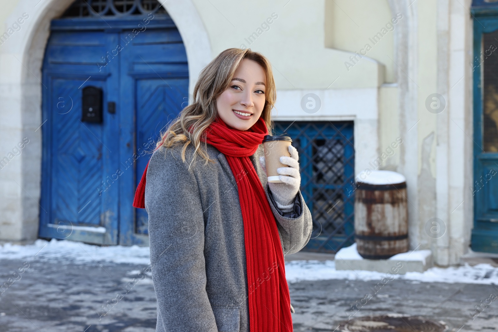 Photo of Portrait of smiling woman with paper cup of coffee on city street in winter