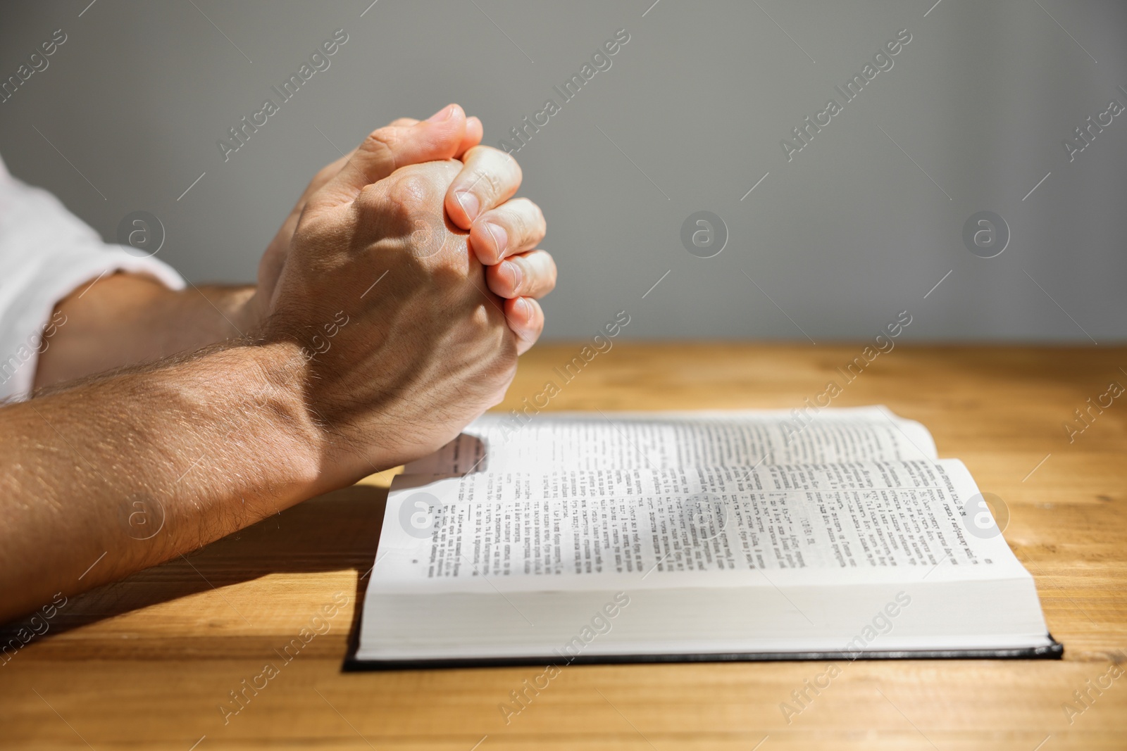 Photo of Man with Bible praying at wooden table, closeup