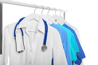 Doctor's gown with stethoscope and different medical uniforms on rack against white background