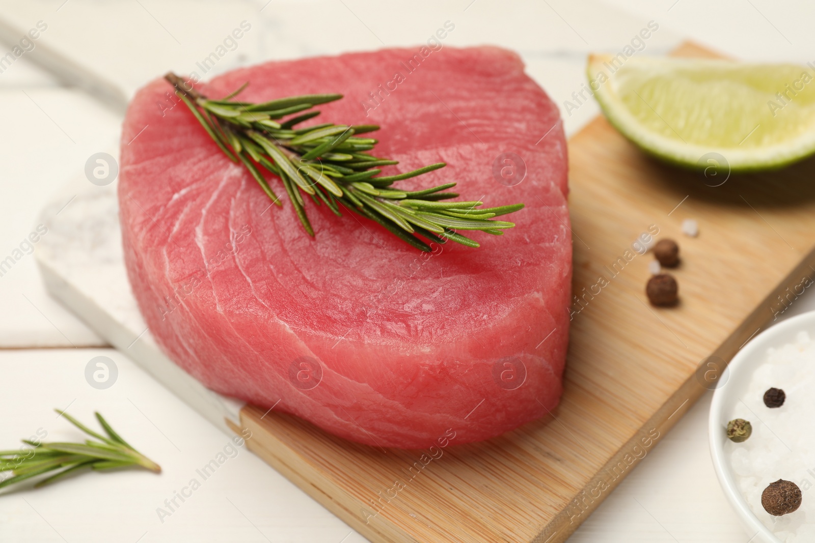 Photo of Raw tuna fillet with rosemary and spices on white table, closeup