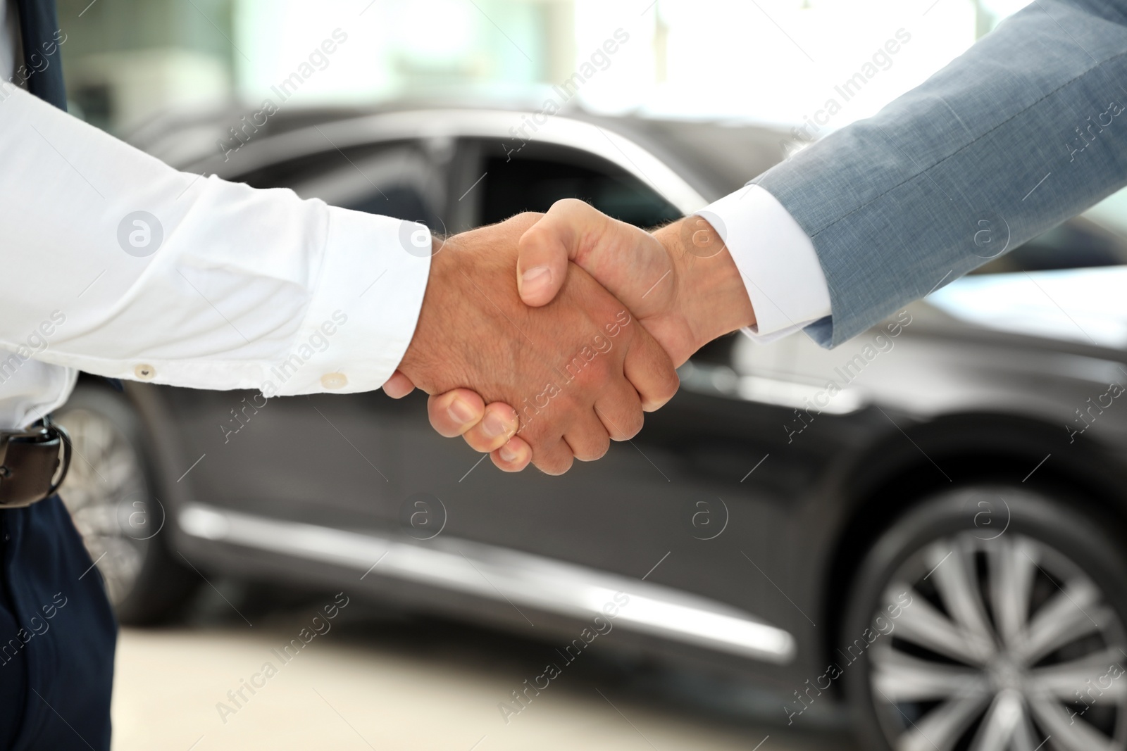 Photo of Young salesman shaking hands with client in modern car dealership, closeup