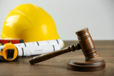 Photo of Construction and land law concepts. Gavel, hard hat, drawings and measuring tape on wooden table, closeup