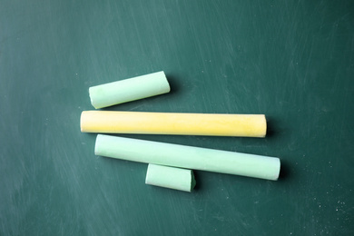 Photo of Pieces of color chalk on greenboard, flat lay