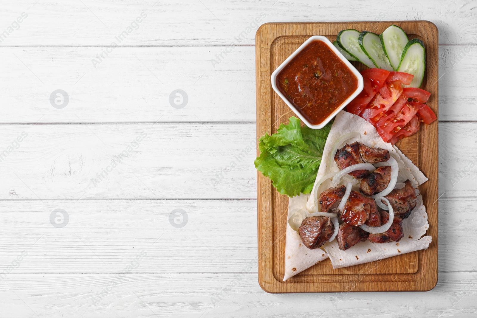 Photo of Wooden board with shish kebab and sauce on table, top view