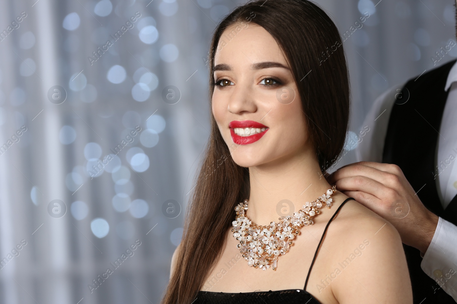 Photo of Man putting jewelry on beautiful young woman against blurred lights, space for text