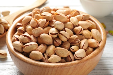 Organic pistachio nuts in bowl on wooden table, closeup